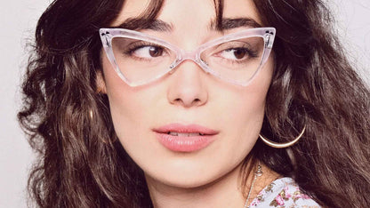 Woman wearing petite blue-light cat-eye glasses and a floral top against a plain background