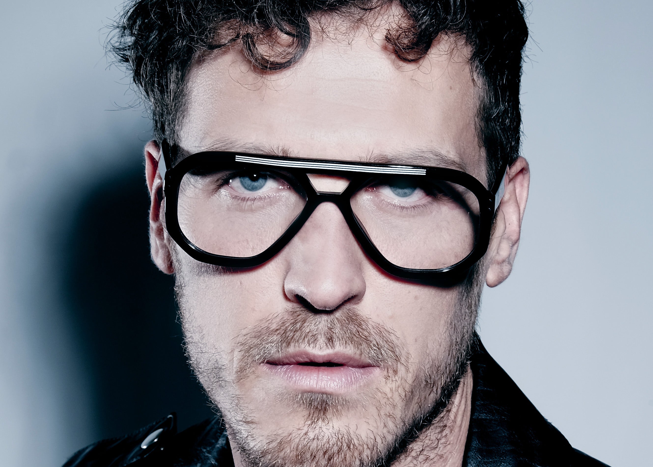 Man wearing black glasses and a leather jacket against a gray background
